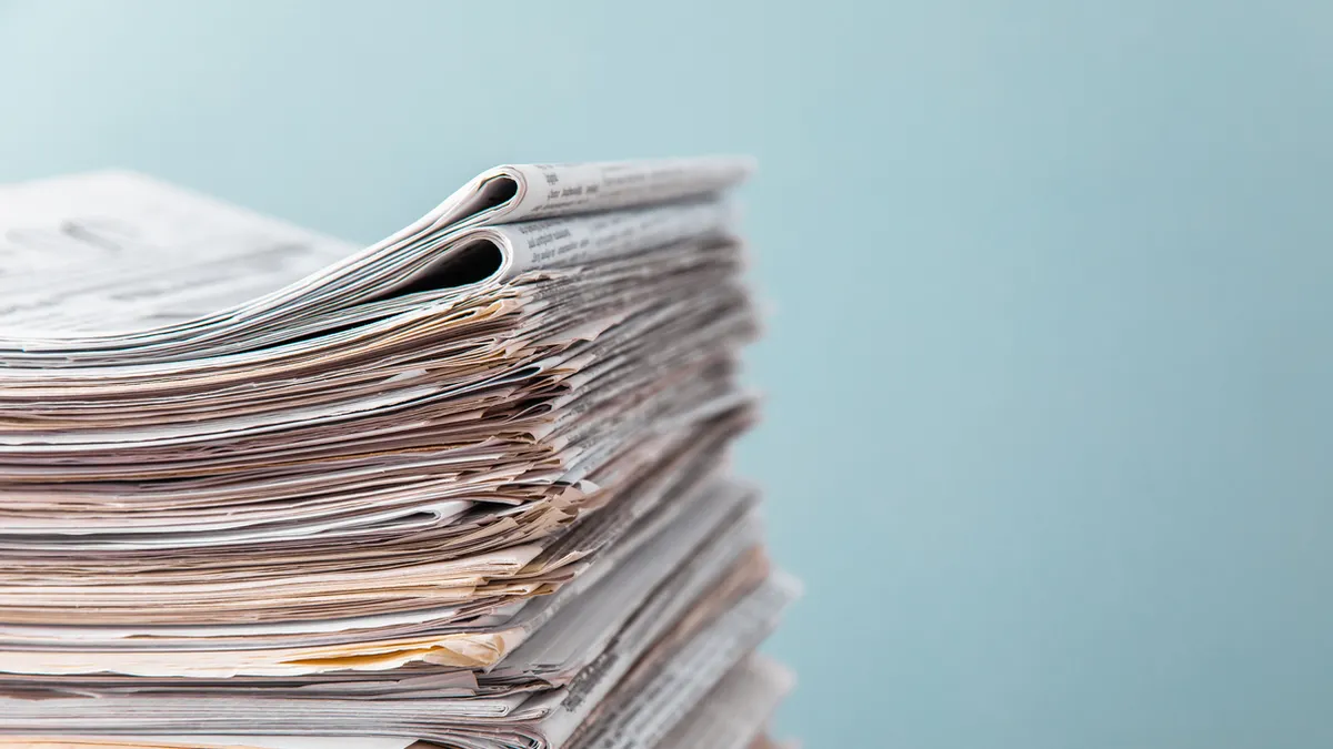 A stack of newspapers are seen against a blue background.
