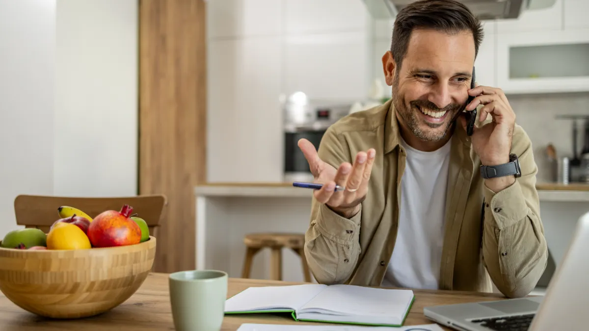 Happy businessman talking on phone and working from home kitchen