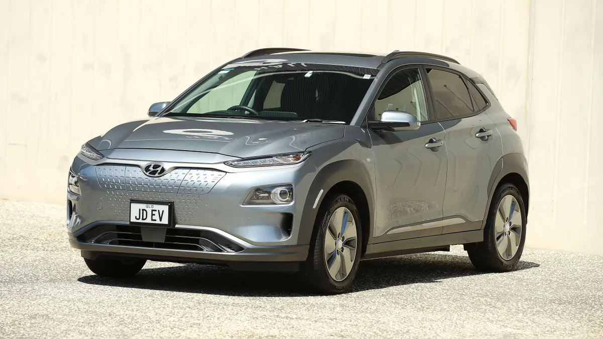 A silver Hyundai Kona Electric Highlander parked under the sun with a beige background.