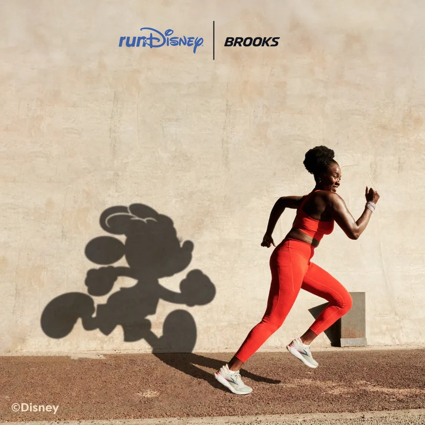 A person running wearing a red two-piece set with a shadow of Mickey Mouse on the wall.