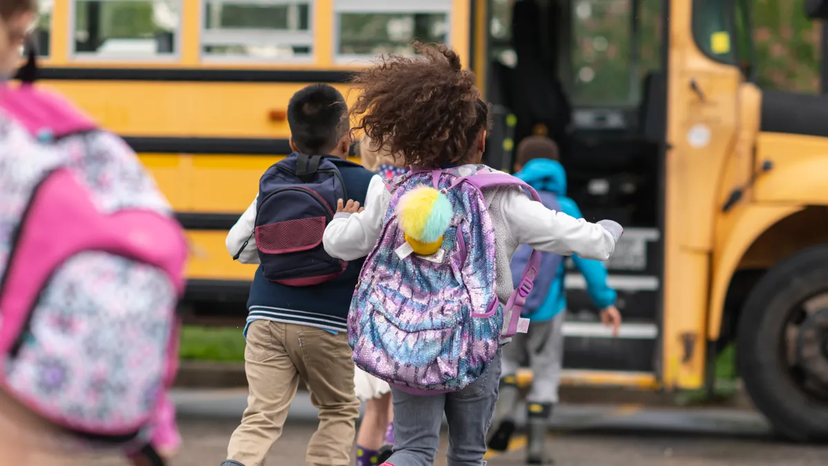 A multi-ethnic group of elementary age children are getting on a school bus.