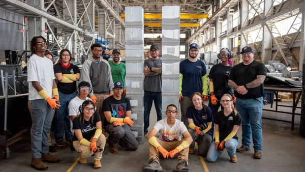 A group of people in safety gear pose in a big metal shop.