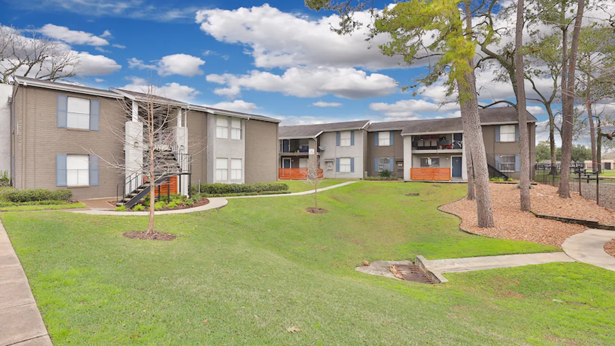 Brown, two-story apartment buildings with grass in the foreground.