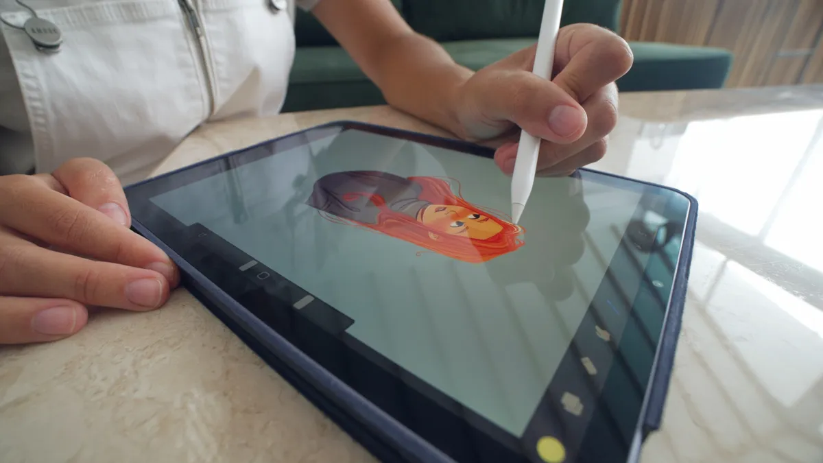 A student designs a fictional character for a video game using a stylus and an iPad.