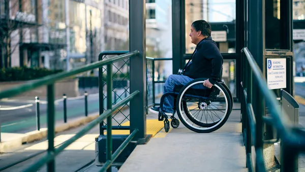 Man in a wheelchair on a ramp at an urban train station.