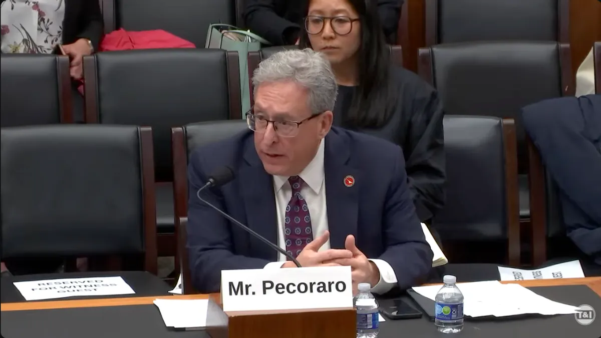 Man seated at a table with rows of chairs behind.