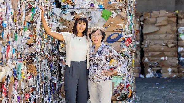 Two women pose near bales of recycled paper