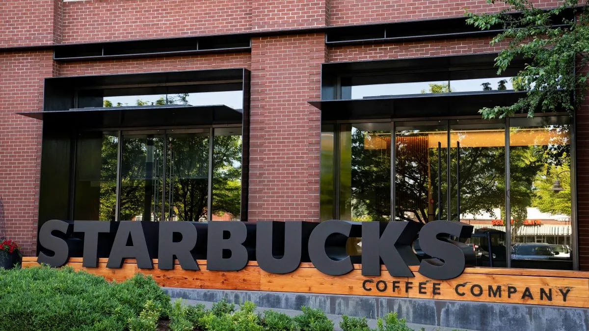 A photograph of a black sign that says "Starbucks Coffee Company" in front of a brick building.