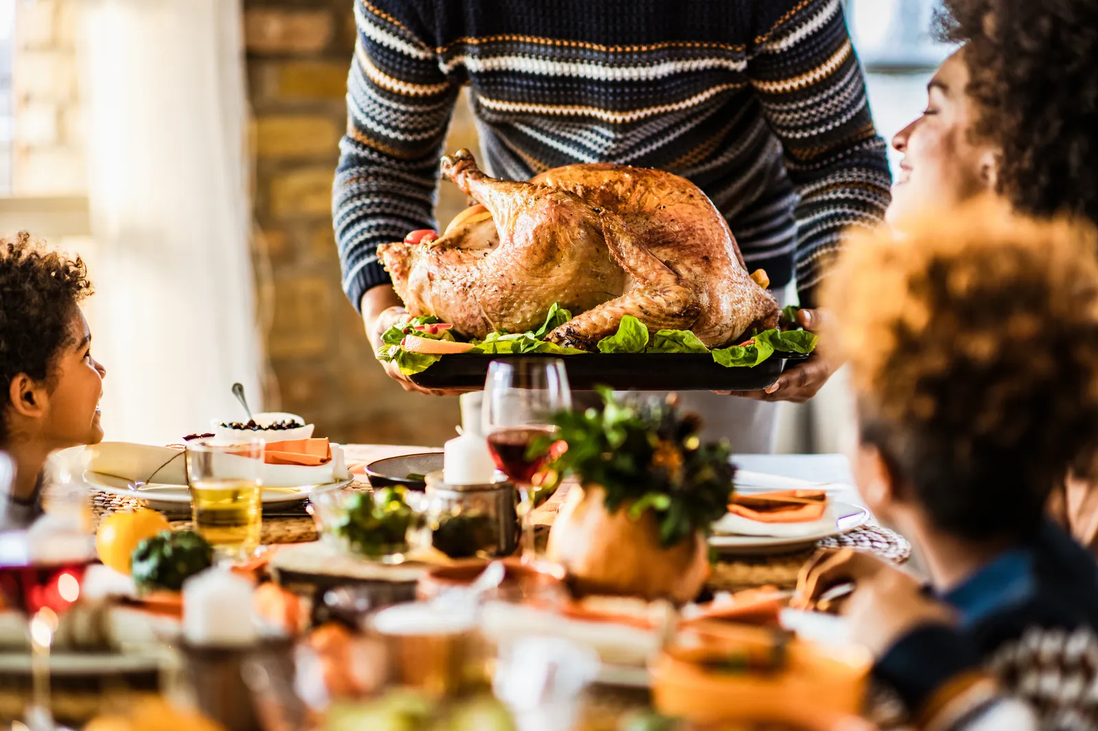 Unrecognizable black father carrying Thanksgiving turkey while serving it for his family in dining room.