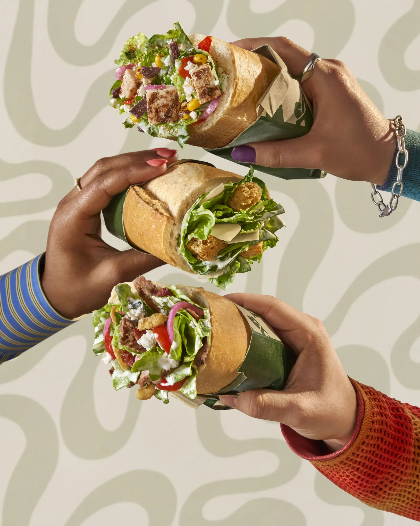 Three hands hold up three rolls with salads inside