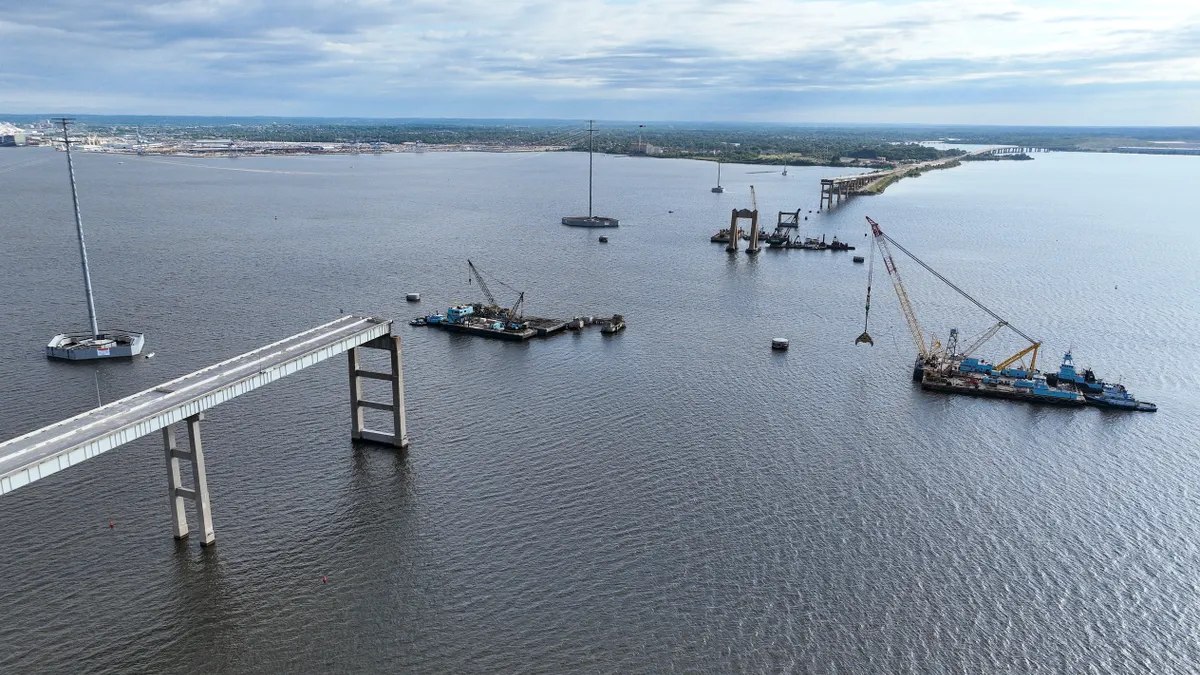 Aerial view shows boats with cranes mounted on them fishing objects out of the water, with a broken bridge on either side.