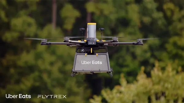 An image of a black drone floating in the air with a green background.