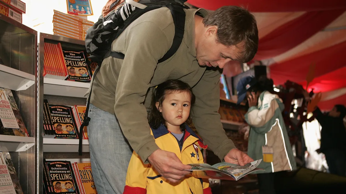 A man bends over to read out of a book while his daughter looks away