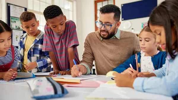 Young school teacher helping elementary students while writing in notebooks