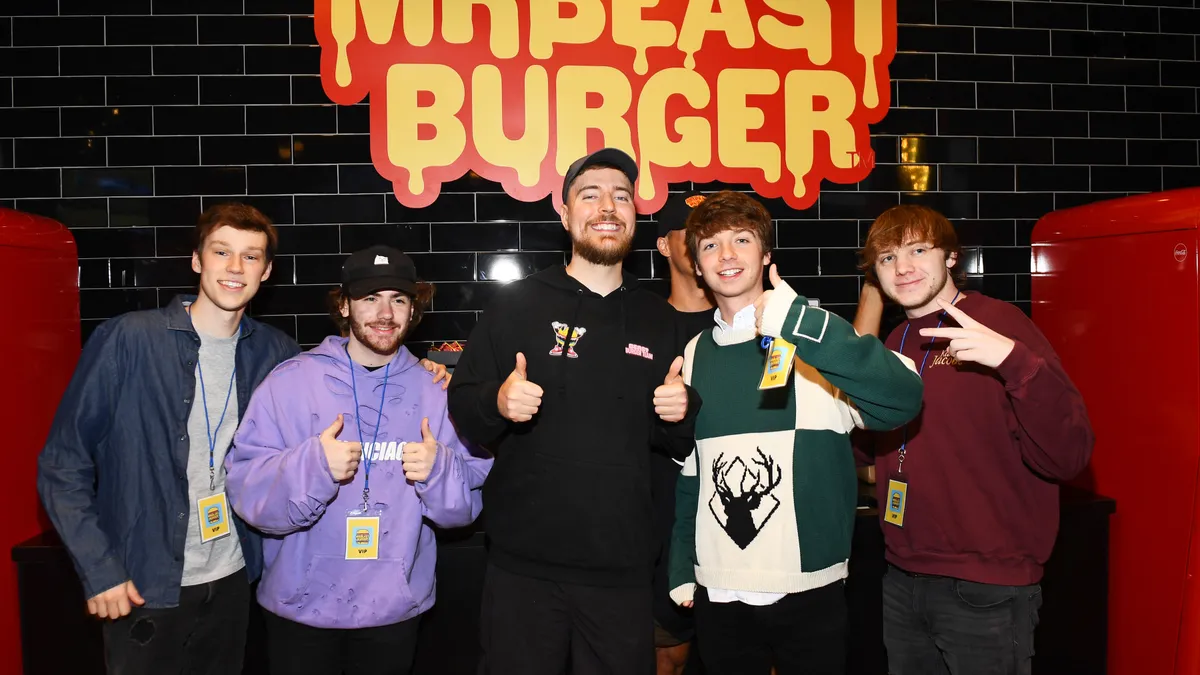 Jimmy Donaldson, or MrBeast, smiles and poses with other influencers in front of branding for his burger chain.