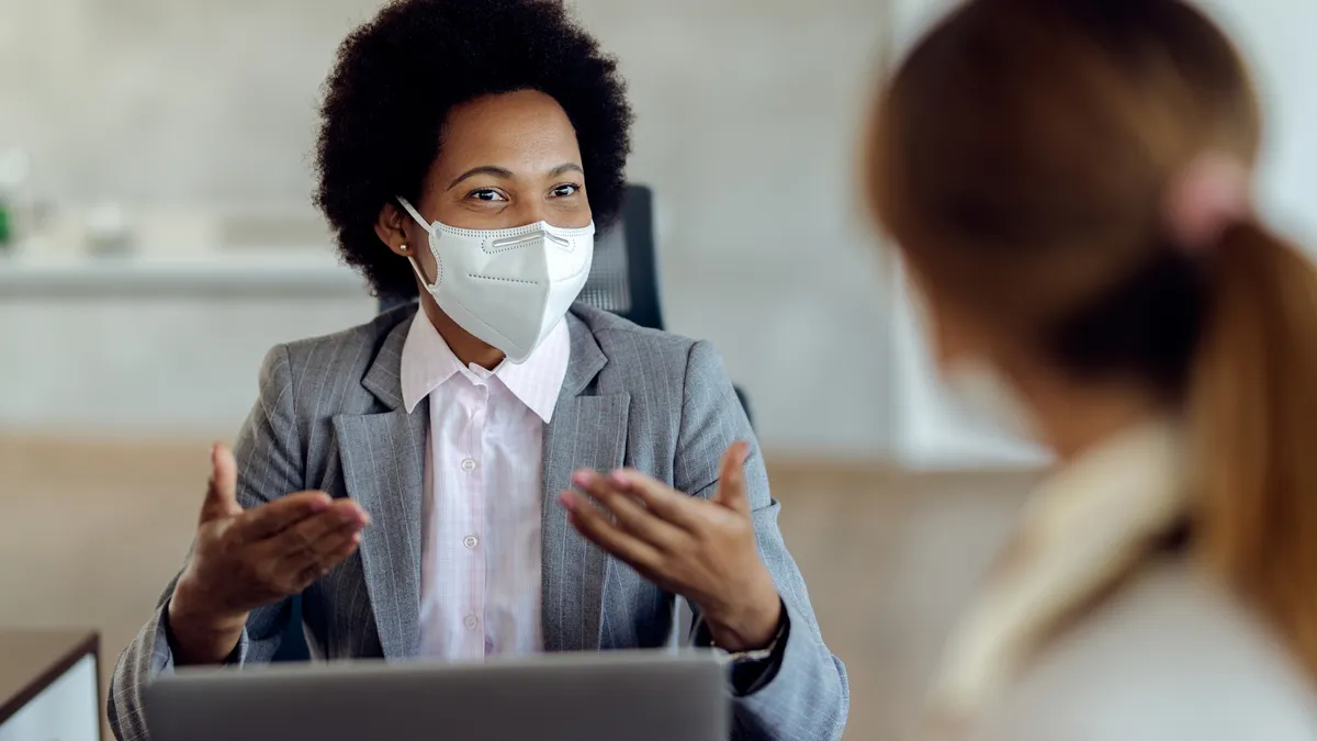 Black female financial consultant talking to her client and wearing protective face mask during the meeting.