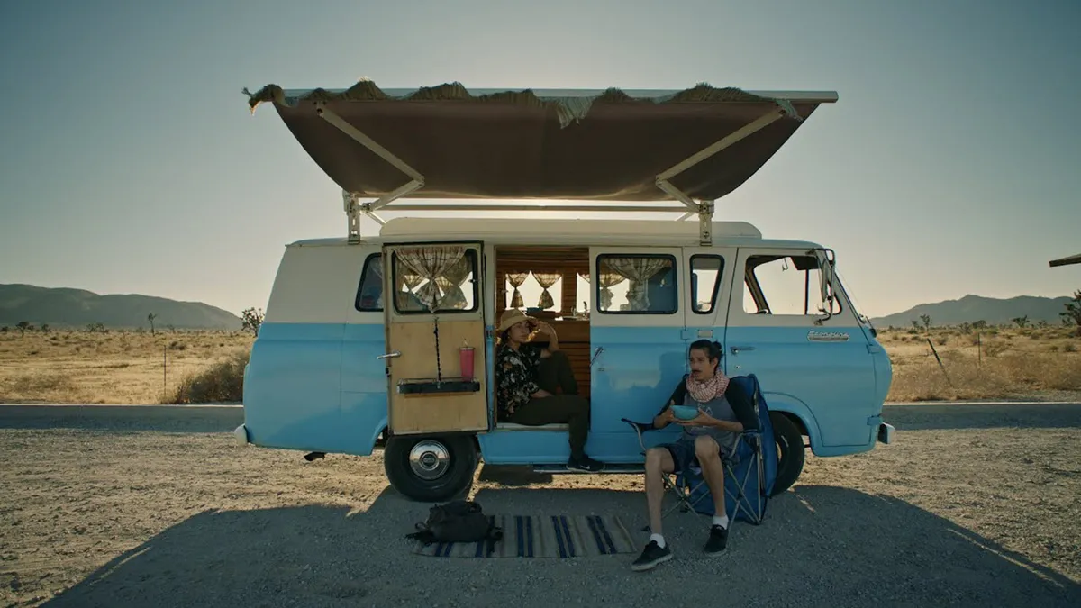 People sitting outside their van in the desert on a road trip.