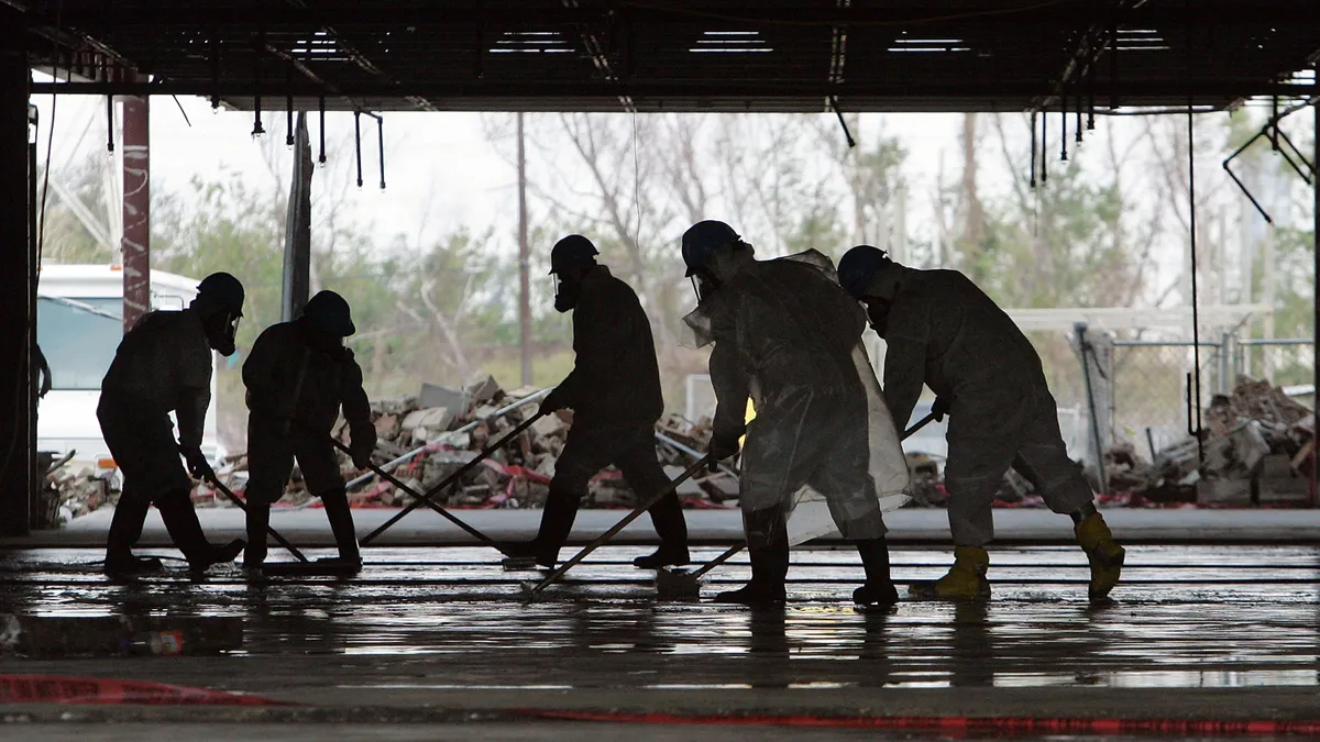 Silhouetted workers in protective suits clean a damaged school following Hurricane Katrina.