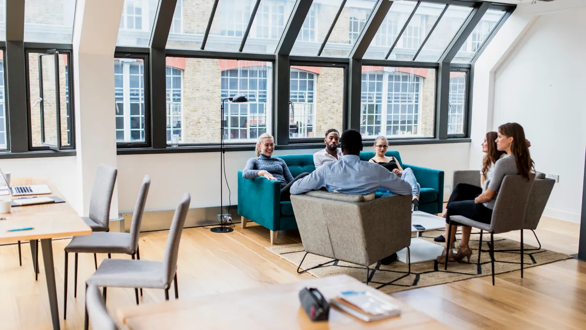 Businesspeople discuss their future plans in the office on a couch and lounge chairs.