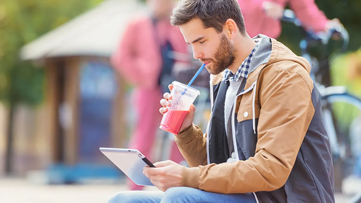 Man drinking a smoothie while looking at ipad