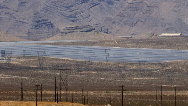 An array of solar panels with transmission lines in a desert.