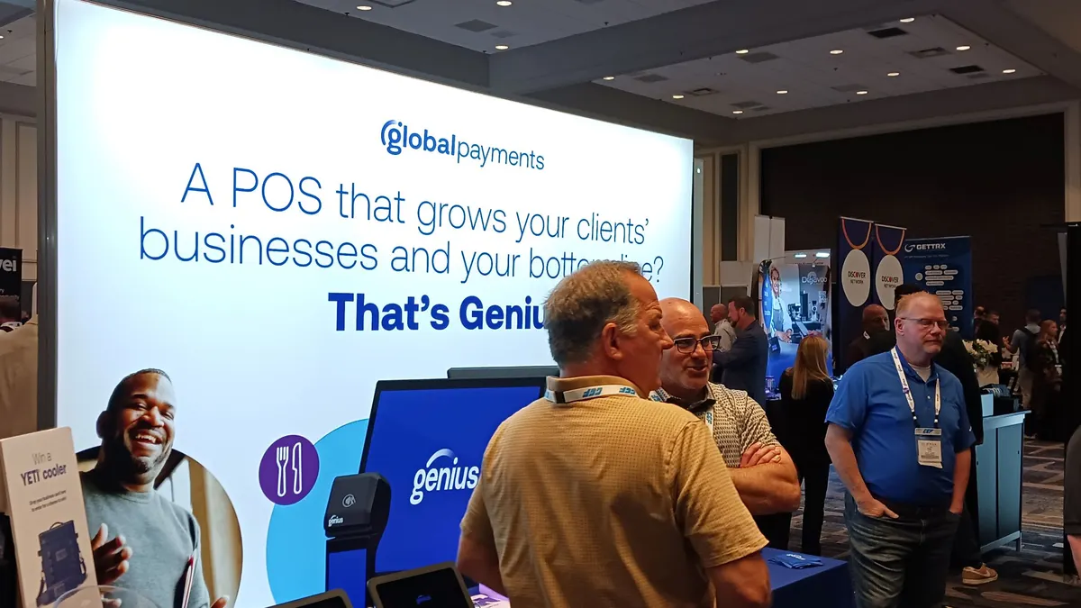 People mill at a conference with a Global Payments sign that markets its Genius brand in the background.