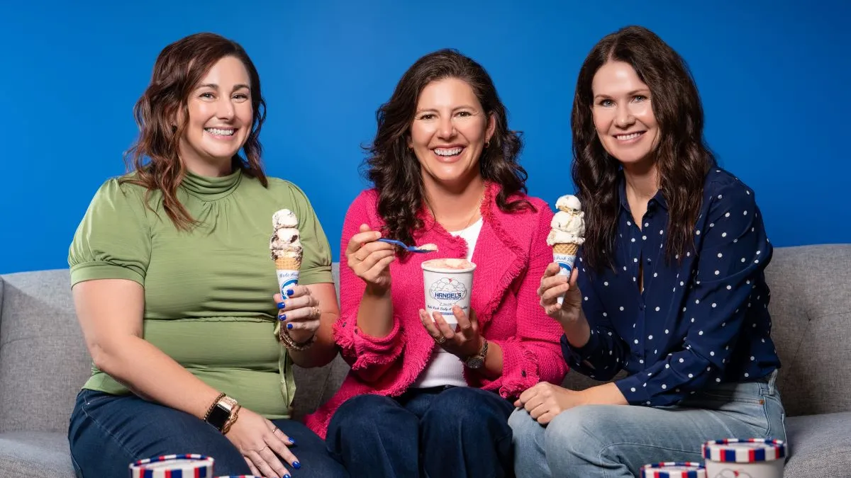 An image of three women sitting on a gray couch. They are each holding up ice cream.