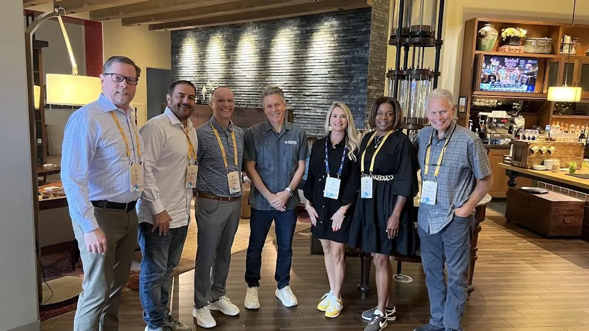 six people in business casual dress stand in a triangular line