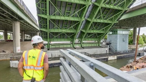 A person in personal protective equipment looks at a bridge over water.