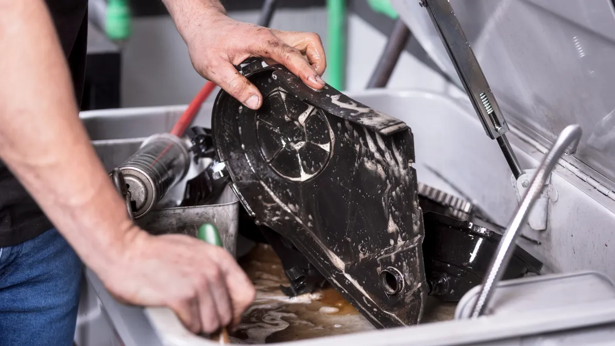 Mechanic'a hands degreasing a car engine part at a service repair station.