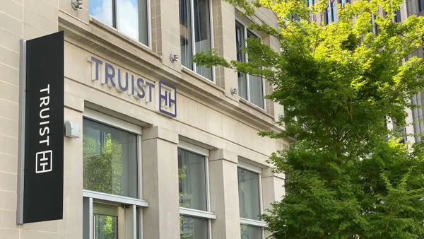 The Truist name is shown vertically and horizontally on a building facade with tree branches on the right side of the frame