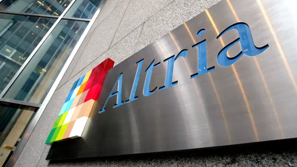 A sign hangs on the side of a buildings. The sign includes a square, multicolored logo and the word Altria.