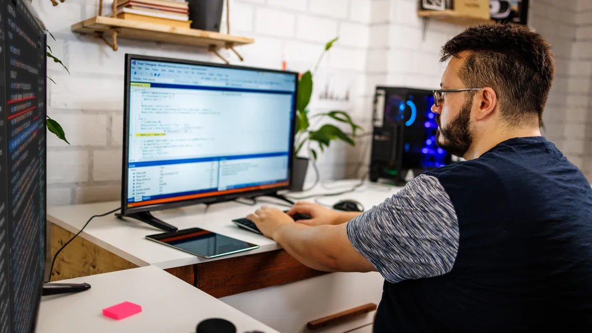 A person sits at a desk, coding on several computer screens.