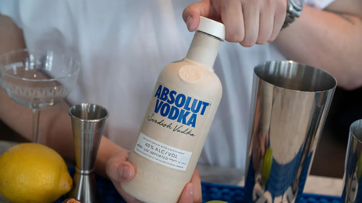 A person's hands open the paper-based cap on a paper-based bottle of Absolut Vodka.