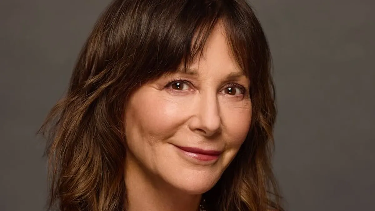 A person with long brown hair smiles.