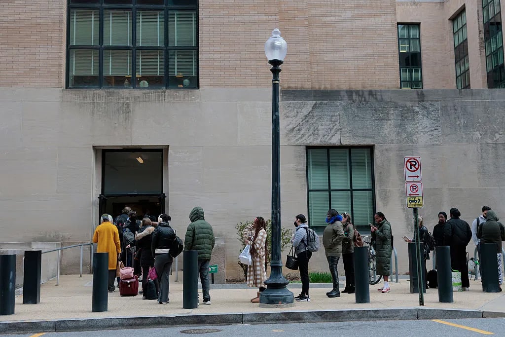A line of people waiting to enter a federal building stretches down the sidewalk