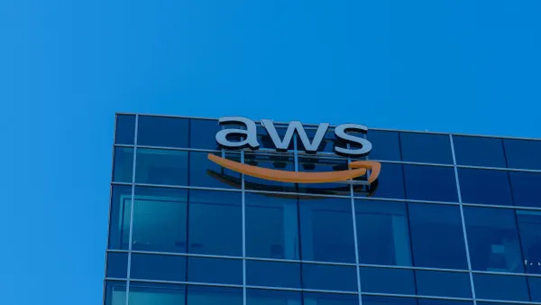 The upper section of a glass office building with a large sign reading “aws” and an orange curved line below the text. The building is set against a bright blue sky.