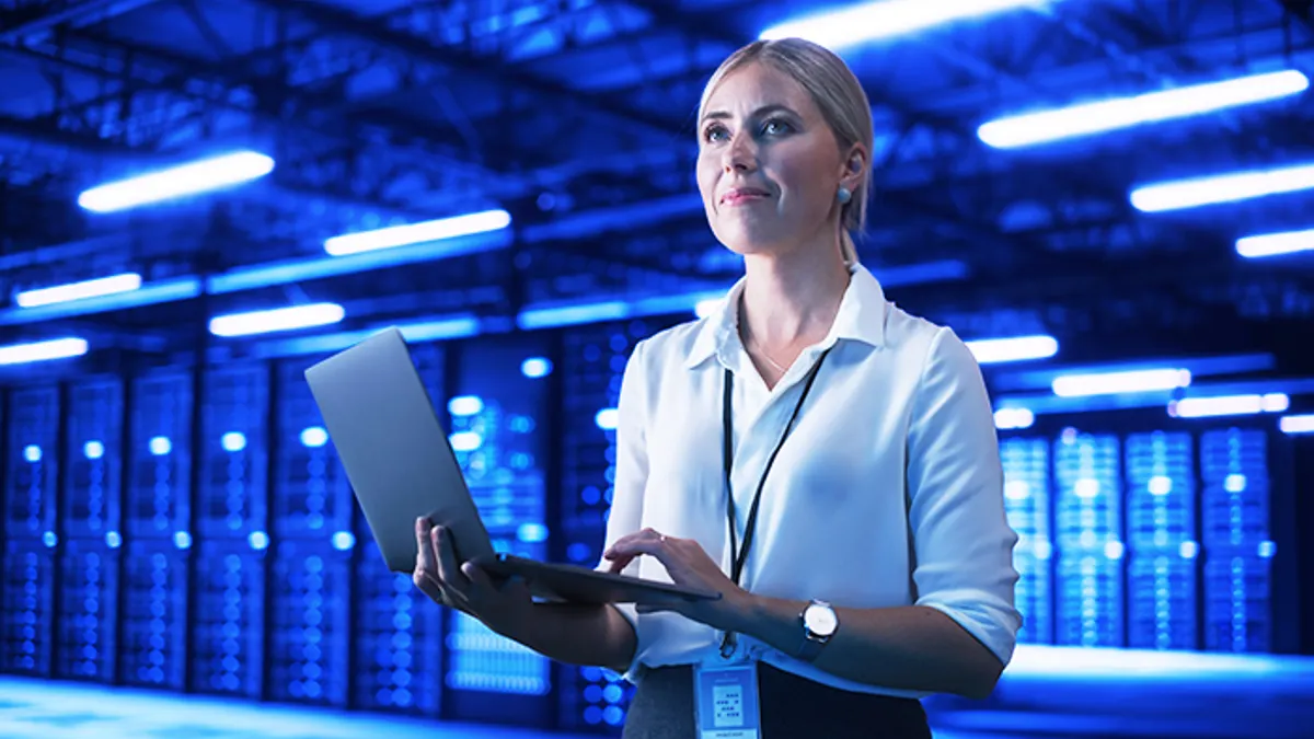 Person standing in a computer control room holding a laptop.