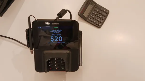 Point-of-sale device, with Adyen and Verifone logos, sits on store counter next to stapler and calculator.