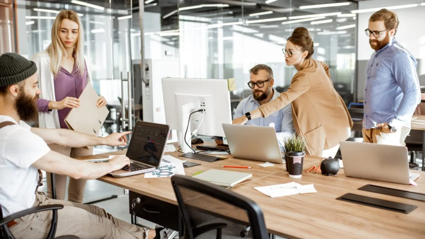 Group of diverse colleagues working on the computers in the modern office or coworking space, bearded hipster as a programmer writing code