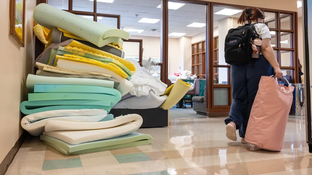 A pile of mattress toppers sits in a hallway, as a person walks by rolling a suitcase, at Boston University