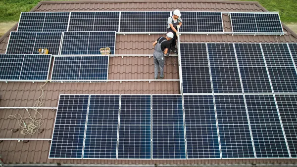 Engineers in helmets install a solar panel system on a roof.