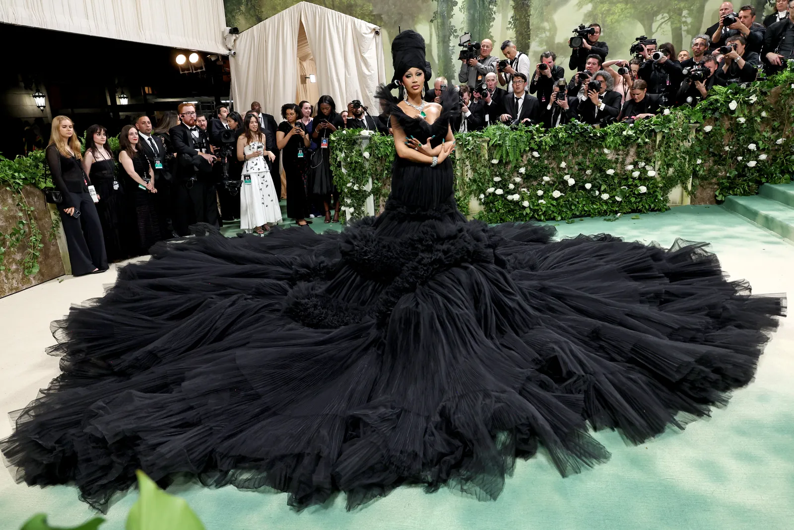 A person wearing an enormous black gown stands in the middle of the frame taking up an entire staircase with her dress.