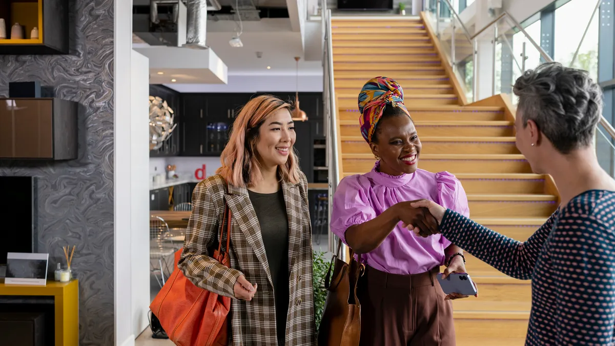 An over the shoulder view of two woman who are meeting with a personal shopper and retail worker who is going to help them choose and design their new kitchen.