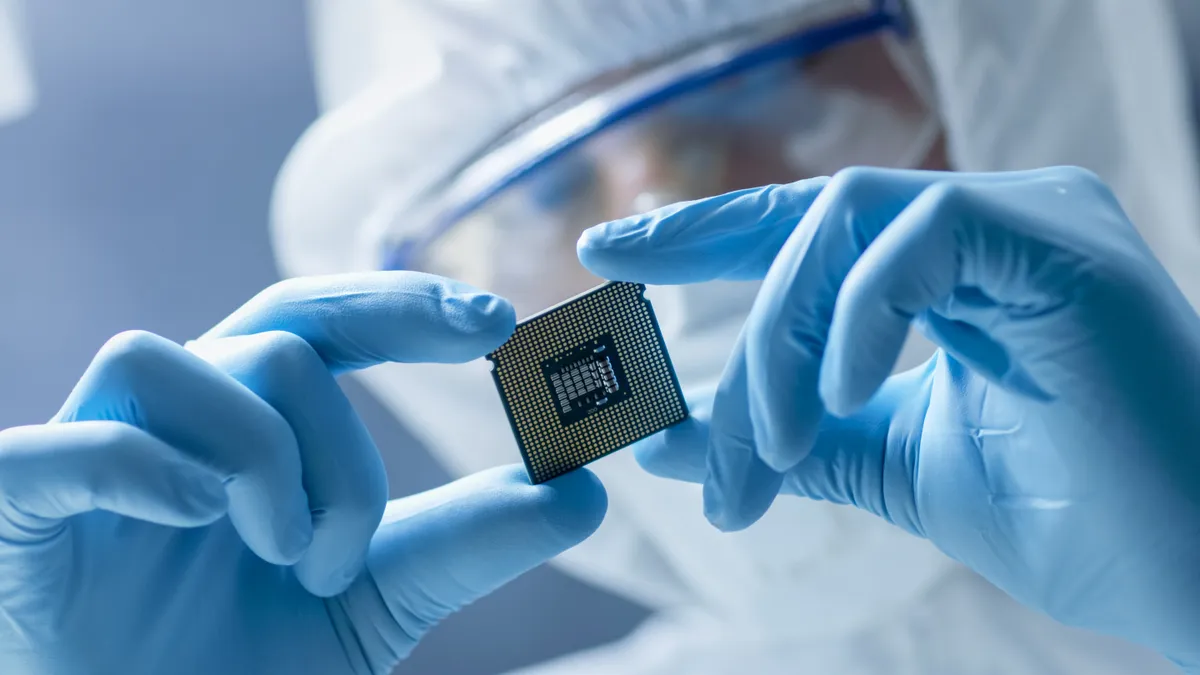 In a moderns electronic manufacturing plant a design engineer in sterile coverall holds microchip with gloves and examines it.