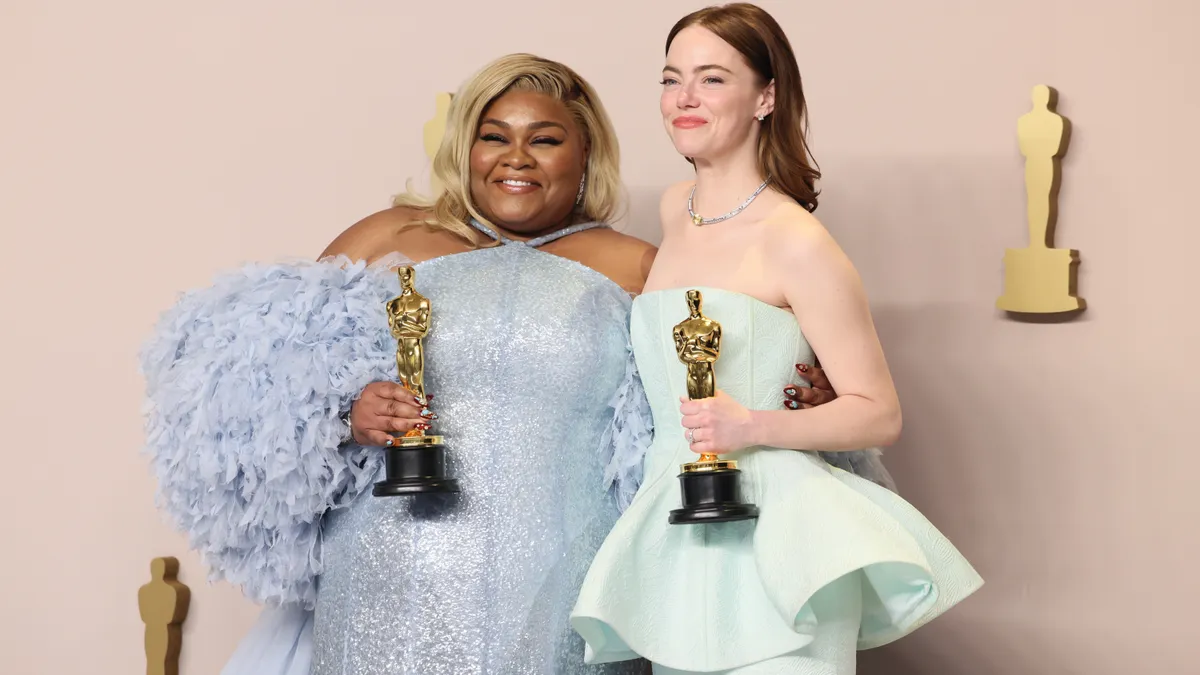 Da'Vine Joy Randolph holding an Oscar wearing a blue gown next to Emma Stone holding an Oscar in a mint gown.