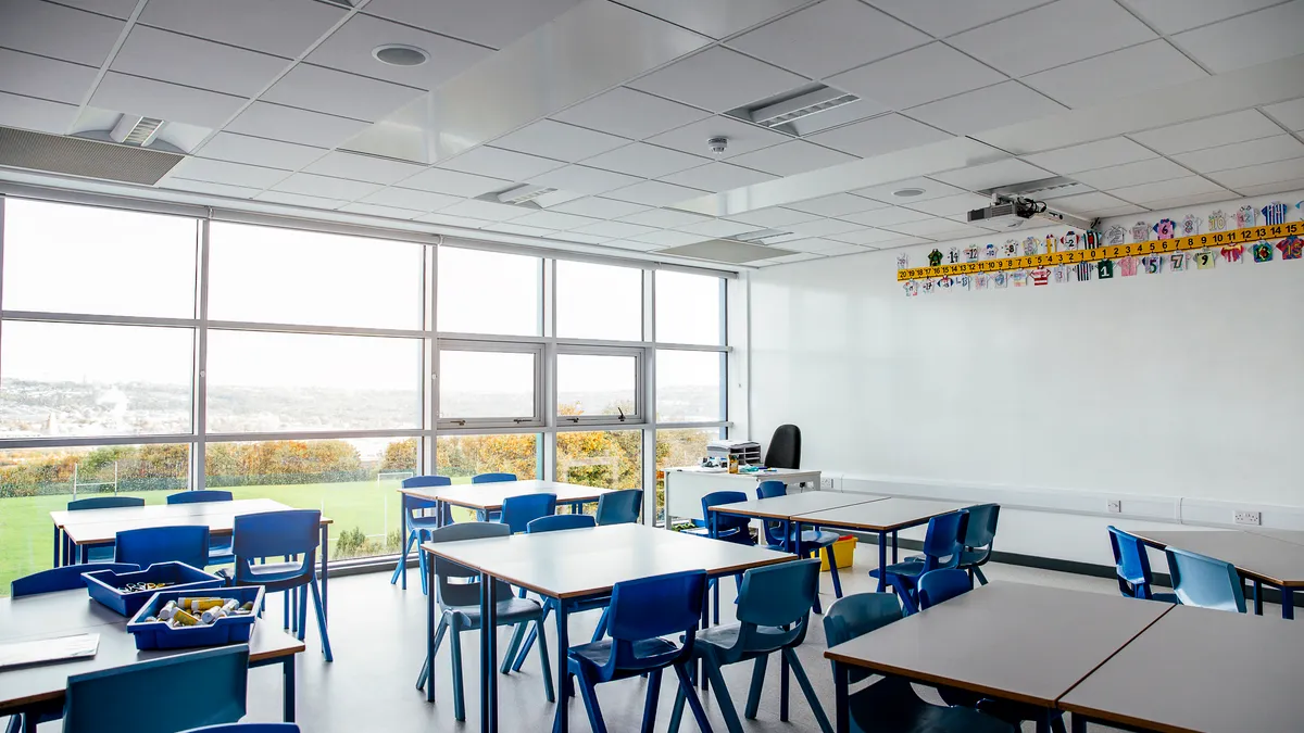 An empty classroom with multiple ceiling air handling units and large windows.