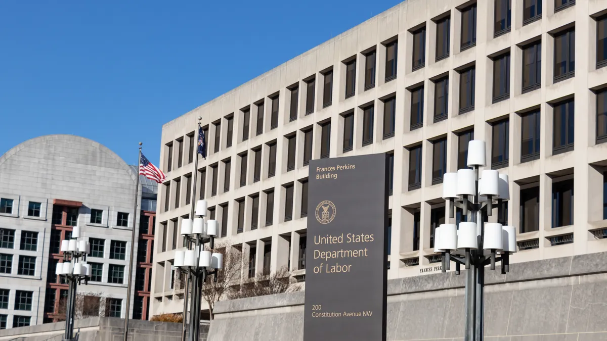 A brown Department of Labor sign in front of a beige building under a clear blue sky.