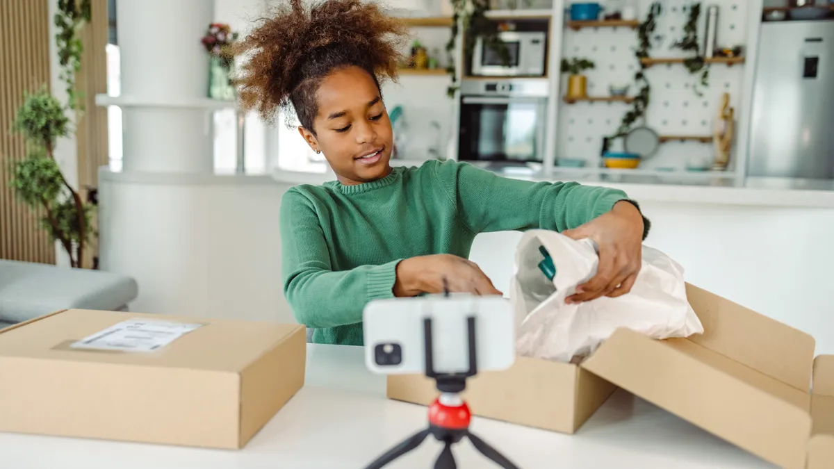 A person opens a box with a product wrapped in filler packaging in front of a video camera.