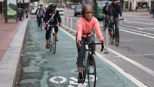 People riding bikes in a bike lane with cars and a bus on the main street.